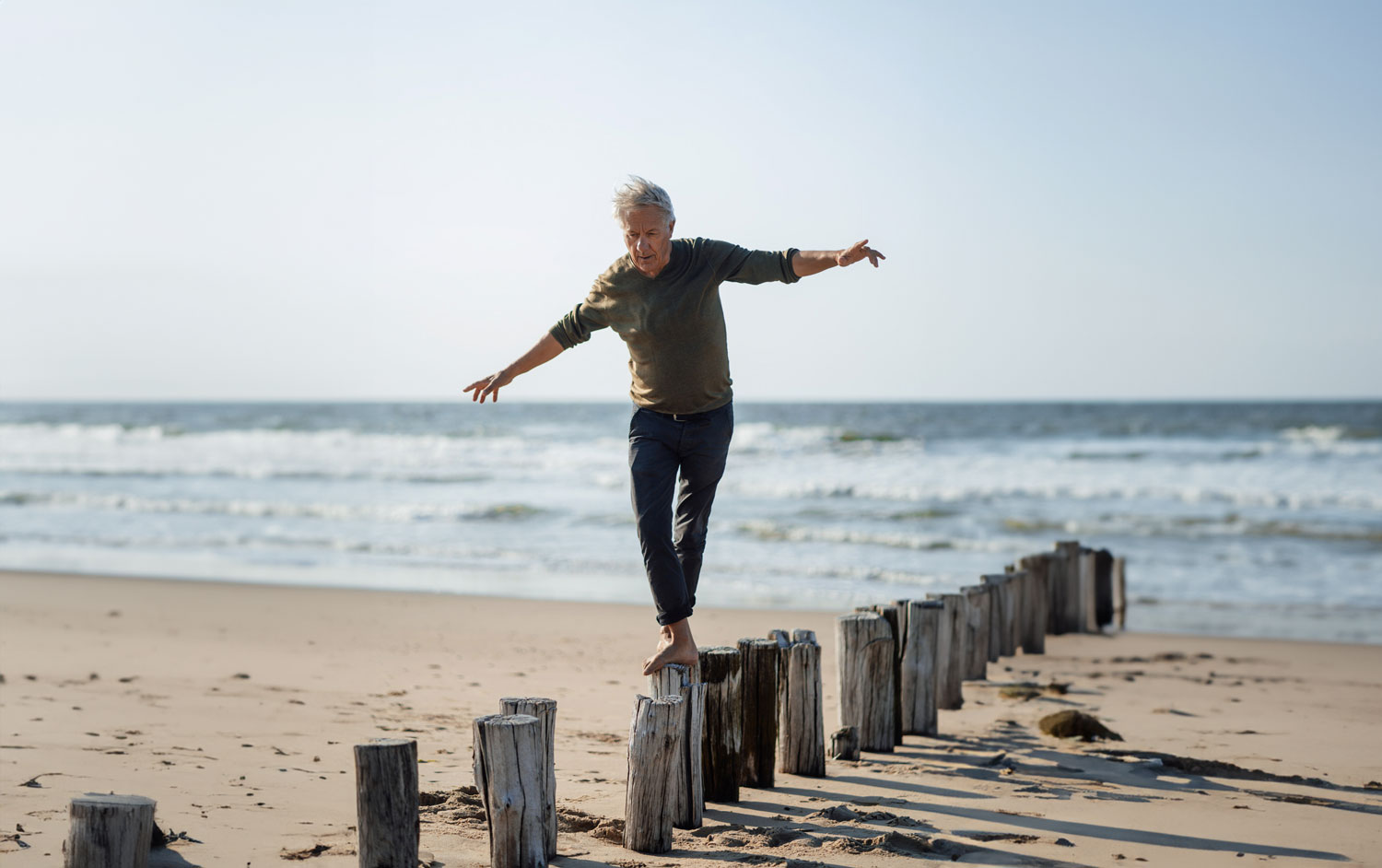 Carefree-senior-man-balancing-on-wooden-posts-at-beach-Recovered Carefree senior man balancing on wooden posts at beach Recovered